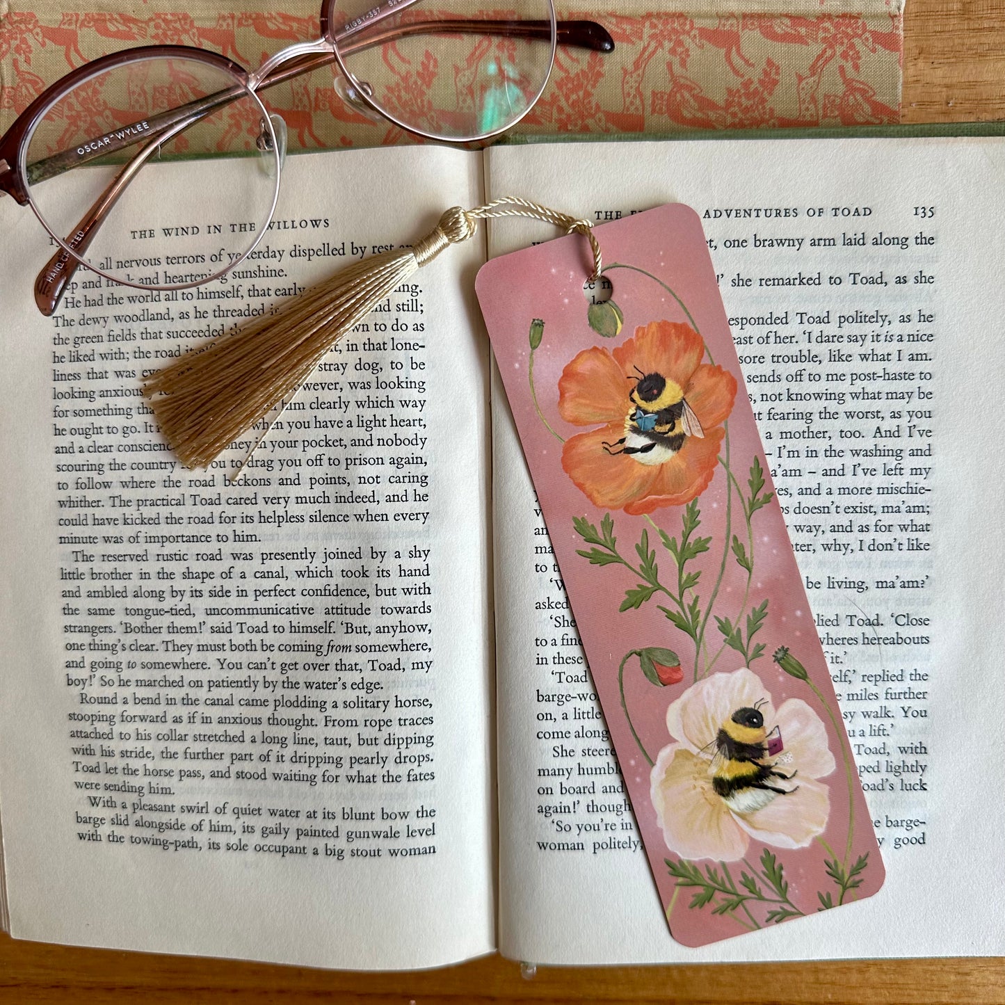 Bumblebee Bibliophiles bookmark by Anna Seed on an open book, bees reading in orange and cream poppies on dusky pink