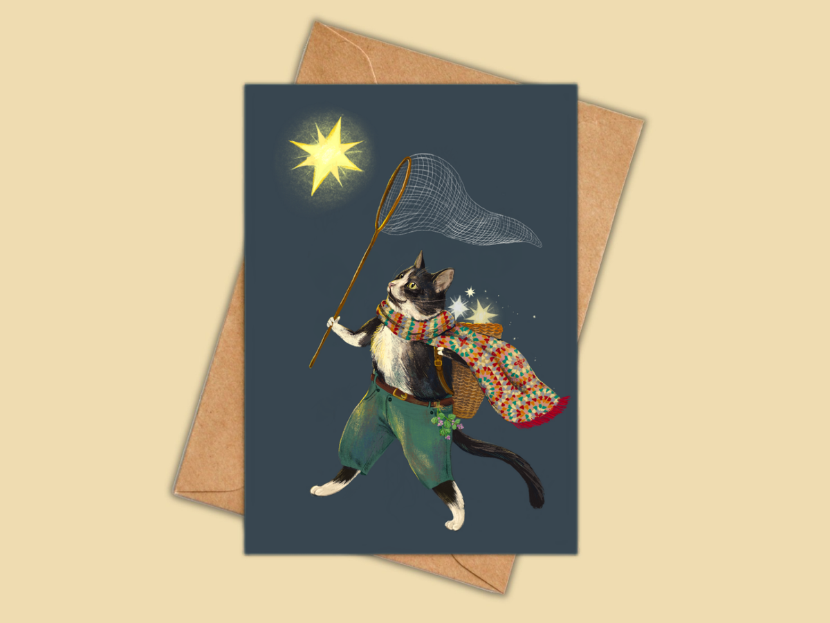 Ashy Cat greeting card by Anna Seed: a cat in a crochet scarf chasing a star with a net, on a kraft envelope