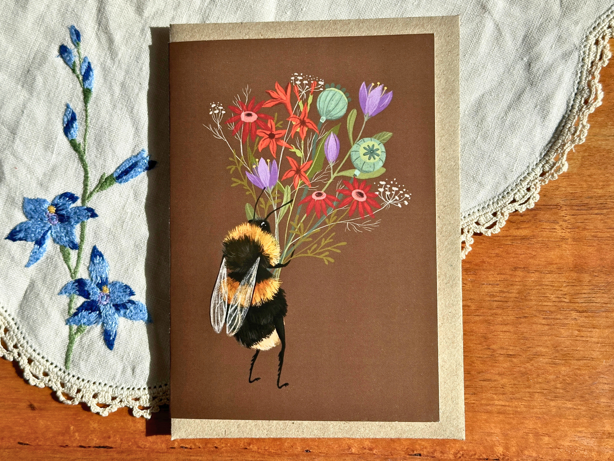 Bee with a Posy greeting card with a bumblebee and wildflowers on brown, on an embroidered doily on a wooden table