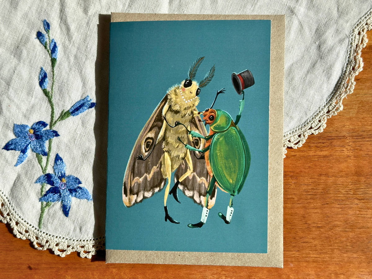 Fancy Dancing greeting card with a moth and top-hatted beetle dancing, on an embroidered doily on a wooden table
