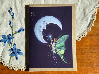 Luna Moth greeting card with a luna moth and sleepy crescent moon, laid on an embroidered doily on a wooden table