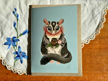 Sugar Glider Teatime greeting card with a glider sipping tea, laid on an embroidered doily on a wooden table