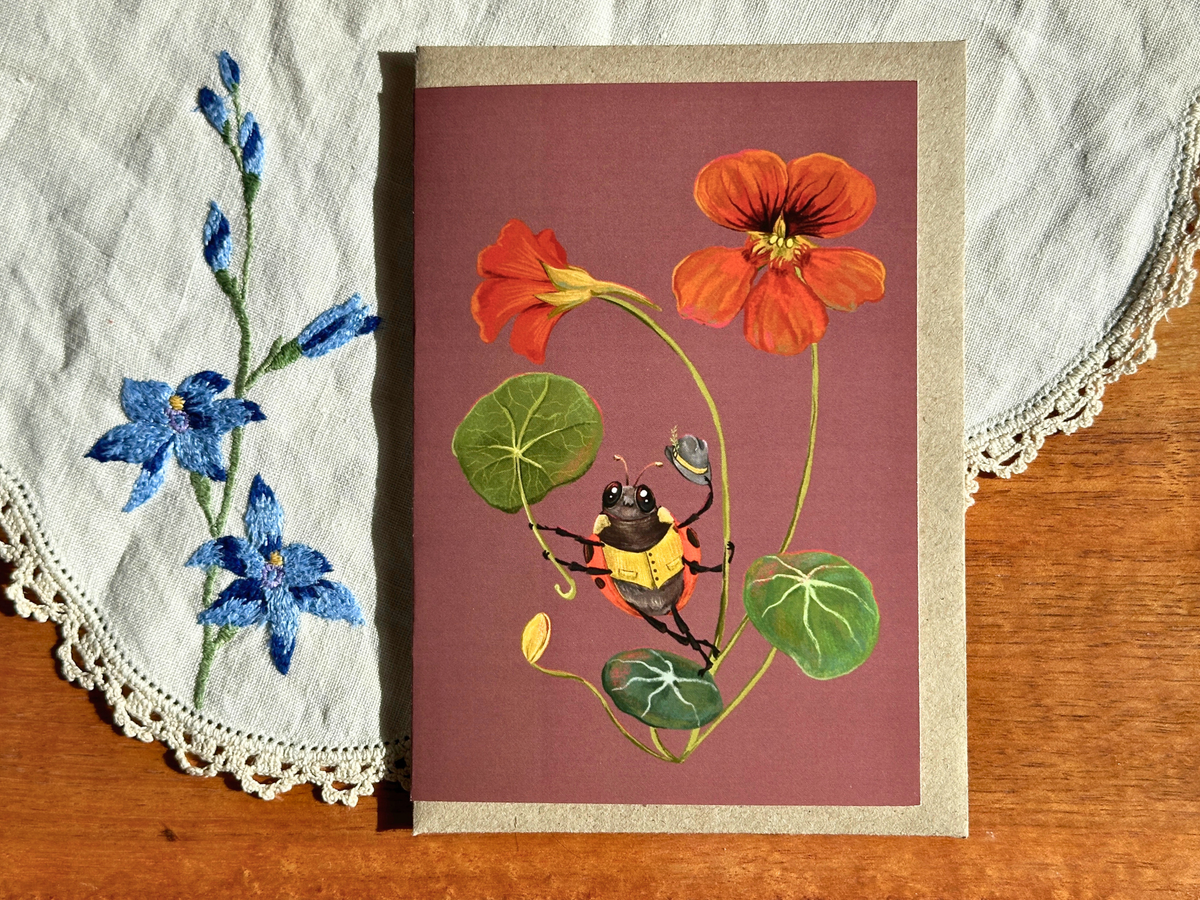 Sunshower greeting card with a beetle among nasturtium flowers, laid on an embroidered doily on a wooden table