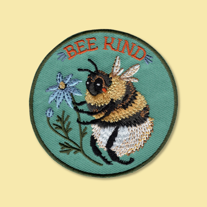 Bee Kind iron-on patch by Anna Seed: an embroidered bumblebee hugging a blue daisy on a round teal patch