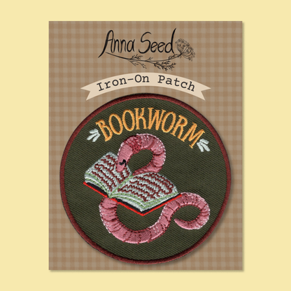 Bookworm patch on its gingham Iron-On Patch backing card, pink worm and open book stitched on a dark green circle