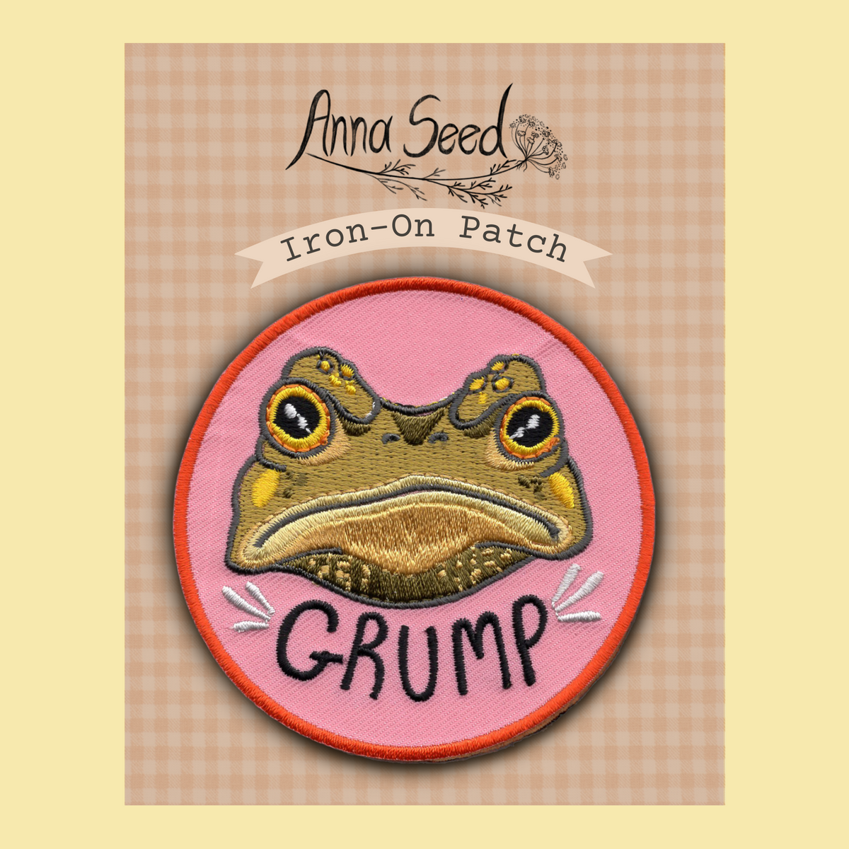 Gustav the Grumpy Toad iron-on patch by Anna Seed: a frowning toad face above the word GRUMP on pink, on its backing card