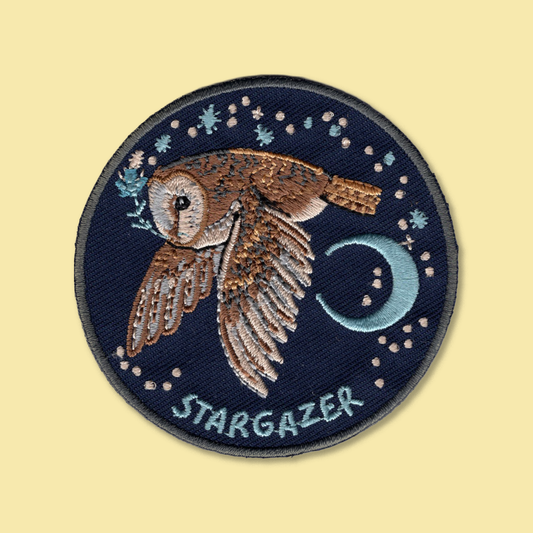 Stargazer iron-on patch by Anna Seed: an embroidered barn owl flying past a crescent moon and stars on navy blue