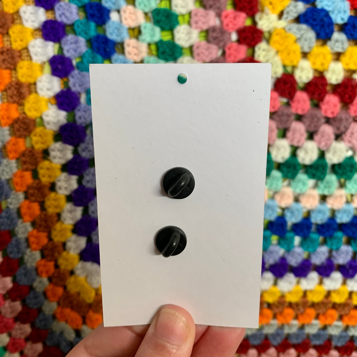Back of the Sweet Radish pin card showing two black rubber clutch backs in a vertical line, against a crochet blanket