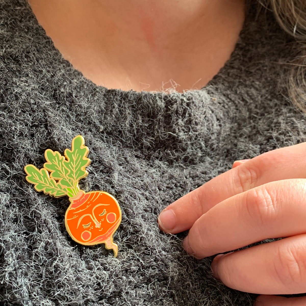 Sweet Radish enamel pin worn on a fluffy charcoal knit jumper, the sleepy-faced orange radish with green leaves