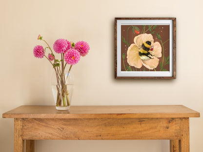 Bee Cosy print of a reading bumblebee in a poppy, framed on a cream wall above a table with pink dahlias