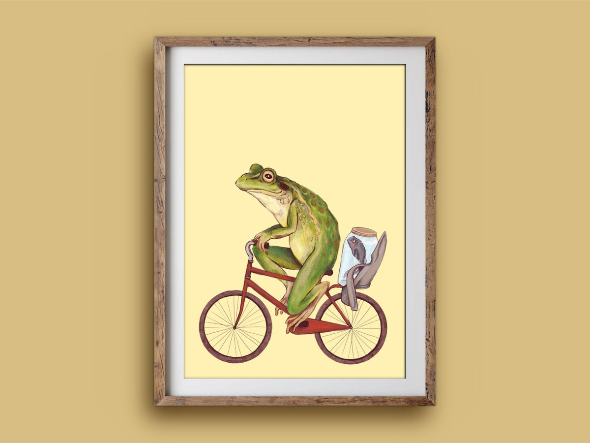 Bicycle Frog art print in a wooden frame, a frog pedalling a red bike carrying a jar, on a mustard wall