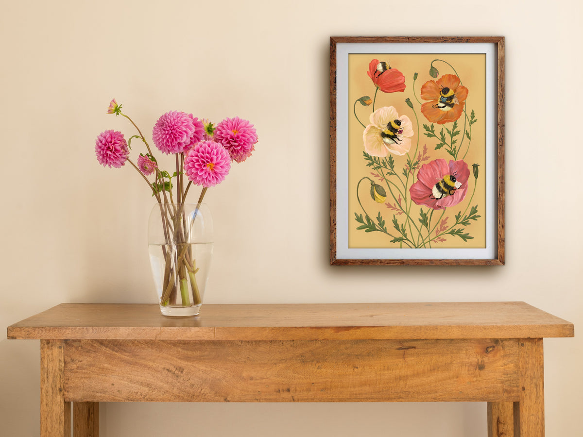 Bumblebee Bibliophiles print of reading bees in poppies, framed on a cream wall above a table with pink dahlias