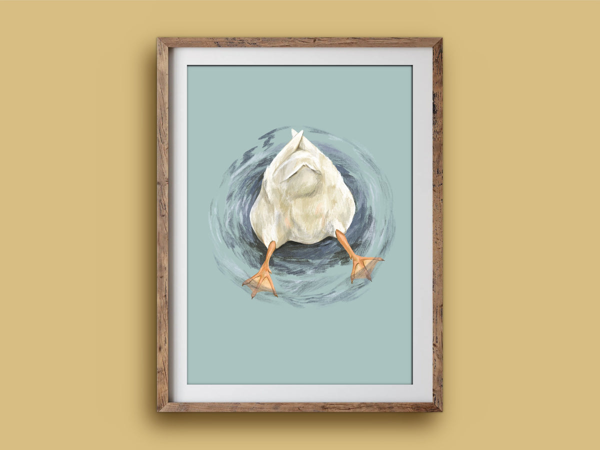 Butt Quack print in a rustic wooden frame on a mustard wall, showing a duck's fluffy bottom and orange feet poking out of the water