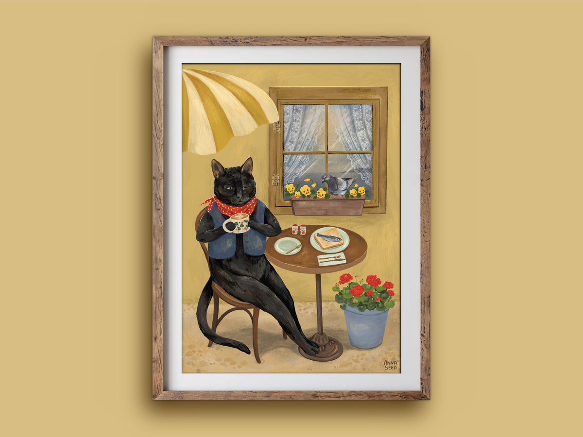 Cat Café print in a rustic wooden frame on a mustard wall, showing a black cat in a waistcoat enjoying coffee and toast