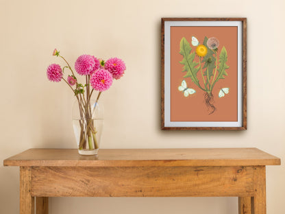 Framed Dandelion print of a dandelion and cabbage moths on burnt orange, hung above a wooden side table with pink dahlias