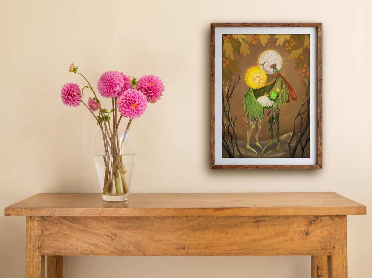 Framed Dandelion Family print of dandelion parents with their baby bud in warm autumn tones, hung above a table with dahlias