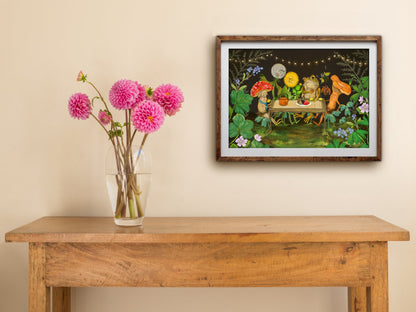 Framed Garden Party print of a toad and mushroom friends sharing tea under string lights, hung above a table with dahlias