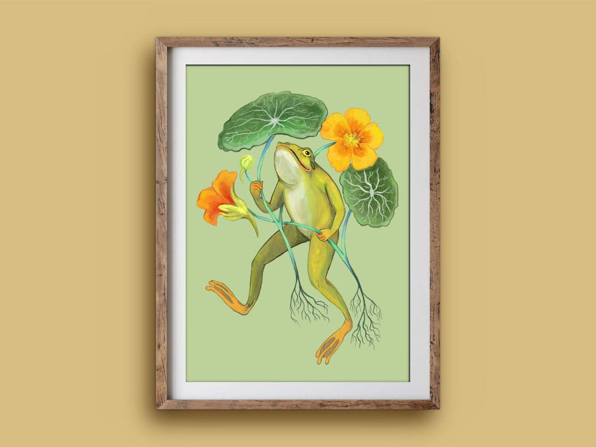 Happy Frog print in a rustic timber frame: a green frog carrying nasturtium flowers and round leaves, on an ochre wall