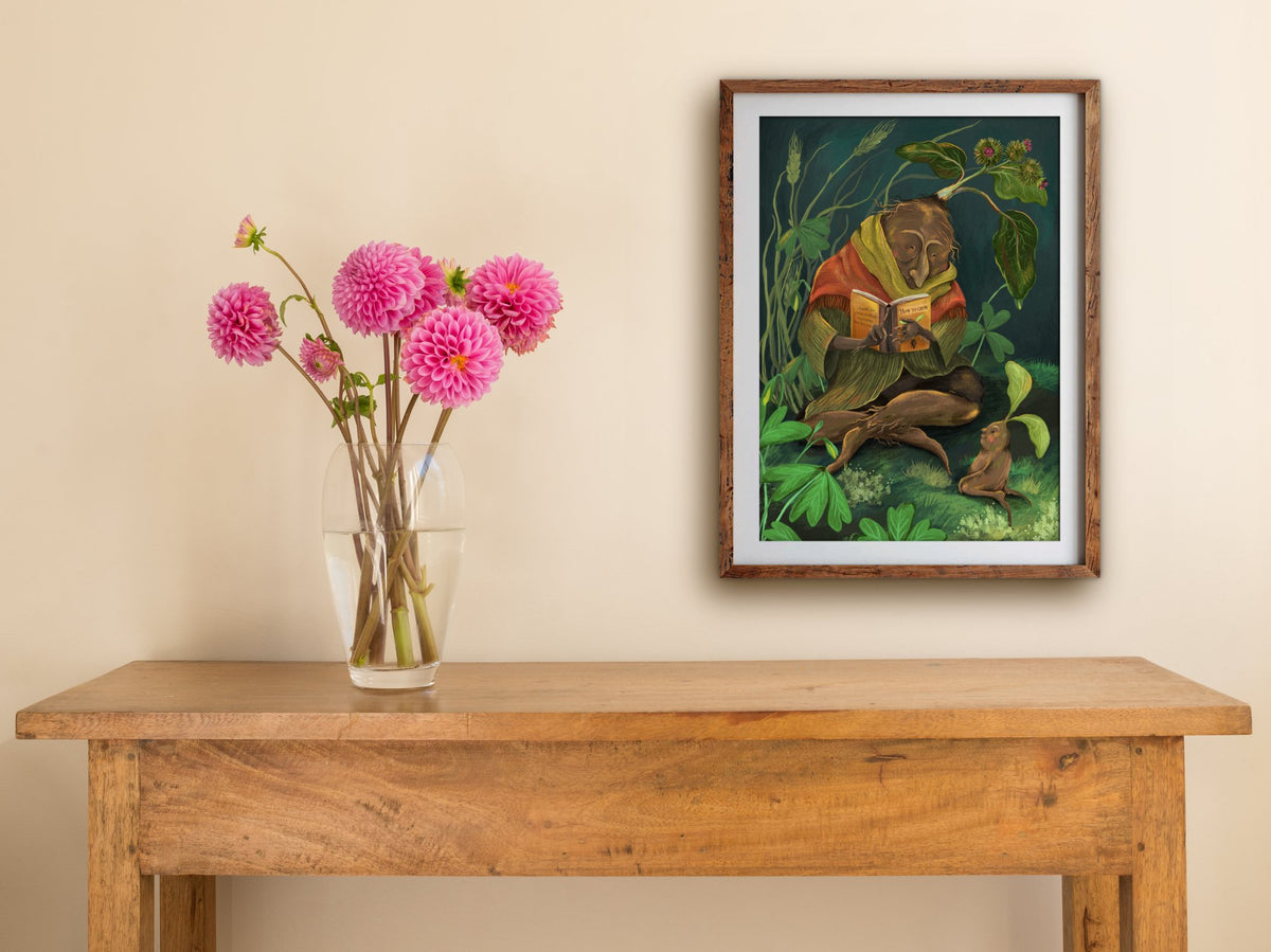 Framed How to Grow print on a cream wall above a wooden side table with a glass vase of pink dahlias