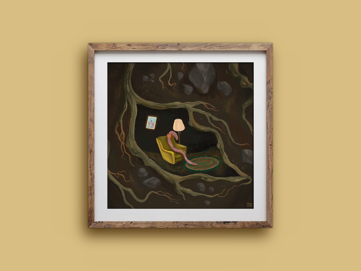 If I Were A Worm print in a timber frame: a pink worm in a cosy armchair with a rug and lamp, nestled among dark roots