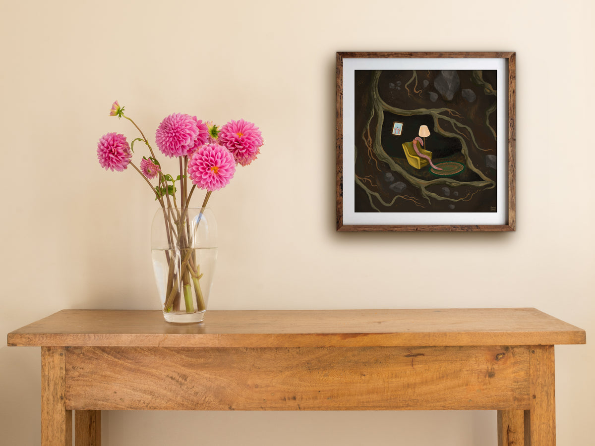 Framed If I Were A Worm print on a cream wall above a wooden side table with a glass vase of pink dahlias