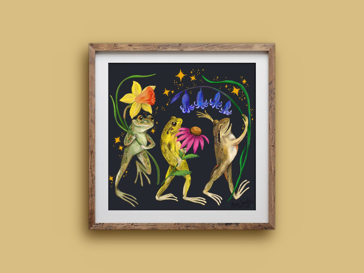 Jolly Frogs print in a rustic timber frame: three dancing frogs carrying spring flowers amid gold stars on dark navy