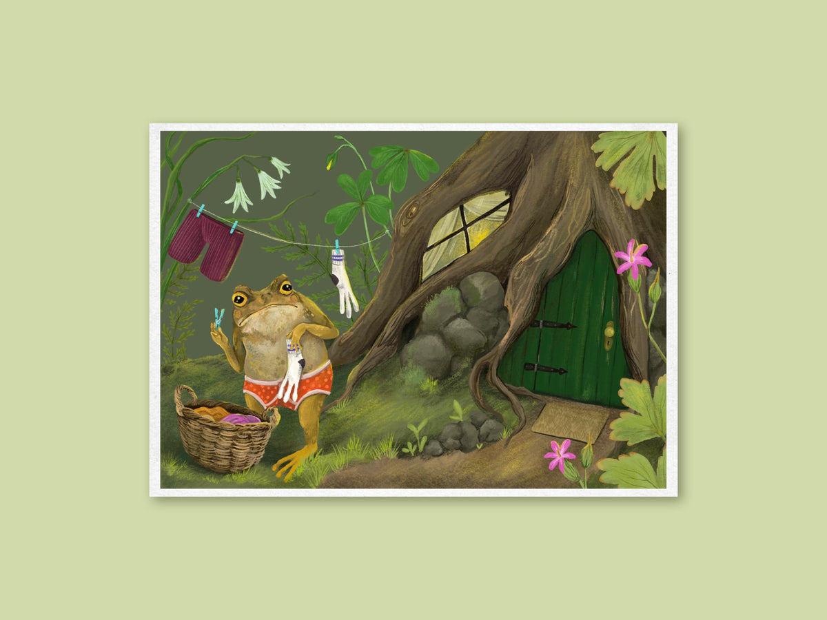 Laundry Toad art print by Anna Seed: a grumpy toad in red undies pegs washing on a line outside his tree-root home