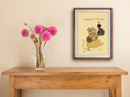 Framed Little Things mouse print on a cream wall above a wooden side table with a glass vase of pink dahlias