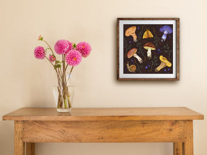 Framed Mushroom Collection print hung above a wooden table with pink dahlias, showing fungi and sparkles on brown