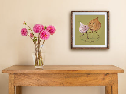 Framed Perfect Together print hung above a wooden table with pink dahlias, showing a dancing garlic and onion pair
