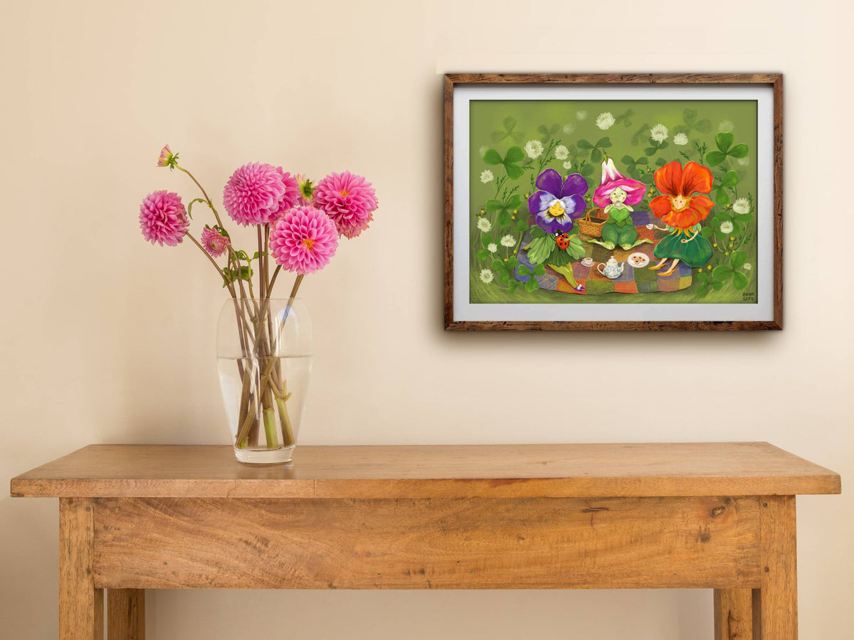 Framed Petal Picnic print hung above a wooden table with pink dahlias, purple, pink and orange flower friends on a rug