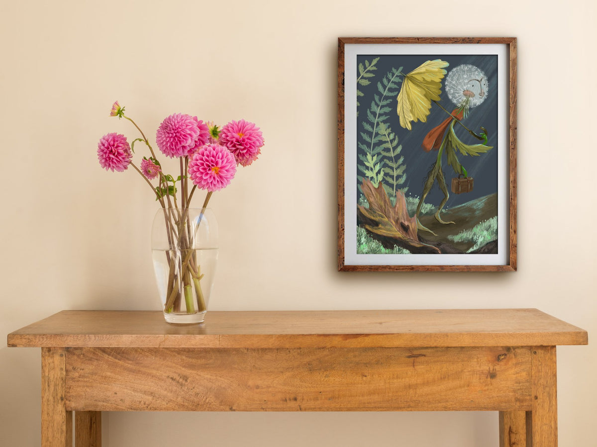 Framed Rainy Day Dandy print hung above a wooden table with pink dahlias, a dandelion walking under a yellow leaf
