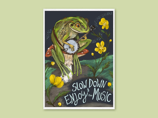 Slow Down art print by Anna Seed: a green frog plays banjo on a toadstool beside buttercups, with 'Slow down & enjoy the music'