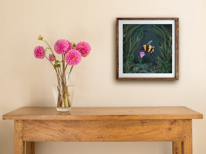 Framed Starflower square print hung above a wooden table with pink dahlias, showing the bee and glowing flower
