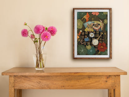 Framed Starry Eyes print hung above a wooden table with pink dahlias, showing the cosy mouse and frog under a blanket