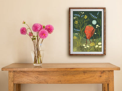 Framed Strawberry Adventurer print hung above a wooden table with pink dahlias, the strawberry among blue and yellow blooms