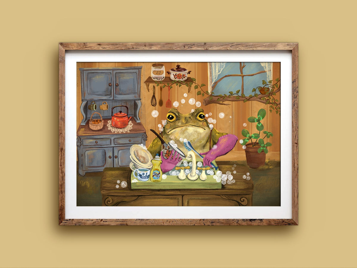 Toady Dishes landscape print in a wooden frame on a mustard wall, a toad at the sink with a red kettle on the dresser