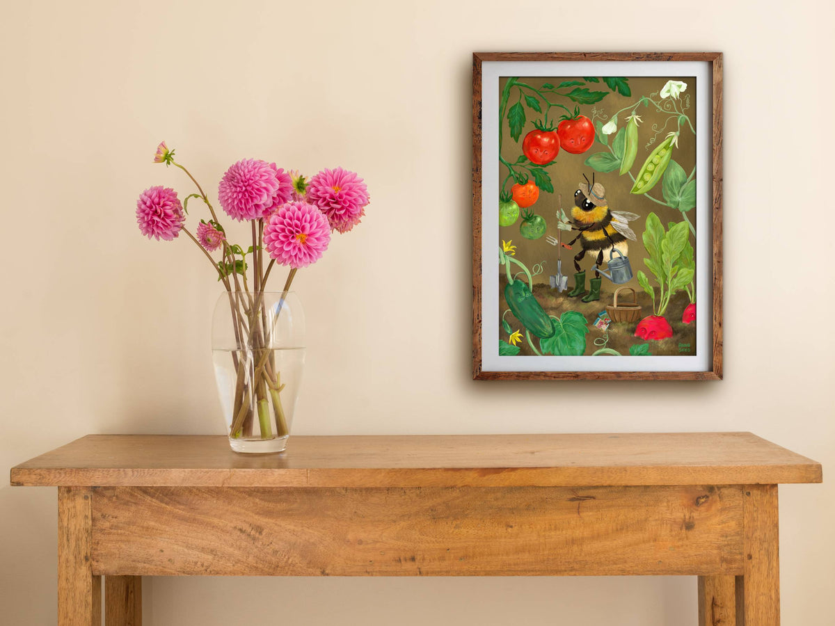 Framed Veggie Patch print hanging above a wooden side table with a vase of pink dahlias against a cream wall