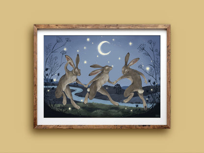 Velveteen Dancers landscape print in a rustic timber frame on a mustard wall, three hares dancing in blue moonlight