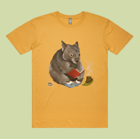 Mustard T-shirt mockup printed with a wombat reading a red book beside a steaming cup, on a pale green backdrop