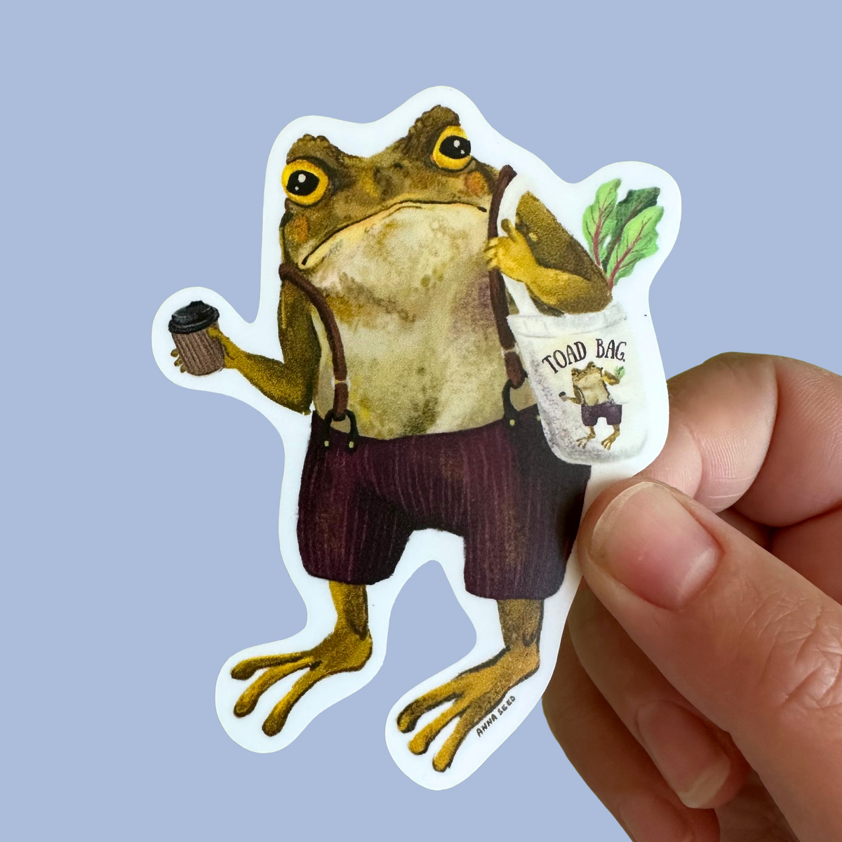 Grumpy Toad sticker by Anna Seed: Gustav the toad in braces with a takeaway coffee and Toad Bag, held on blue