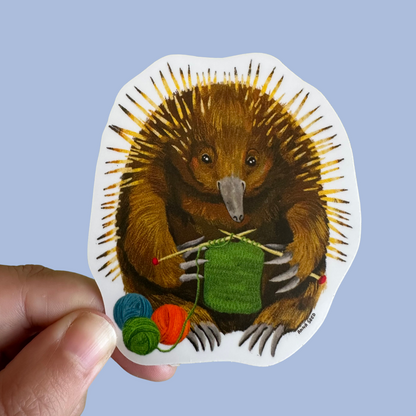 Knitting Needles sticker by Anna Seed: a spiky echidna knitting green wool beside balls of yarn, held on blue