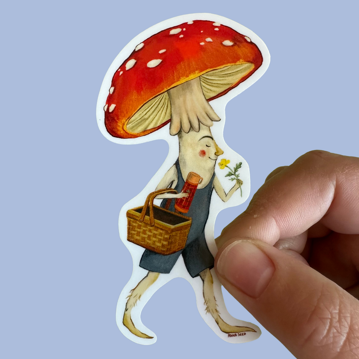 Mushroom Chap sticker by Anna Seed: a red toadstool fellow in overalls with a picnic basket and flower, held on blue