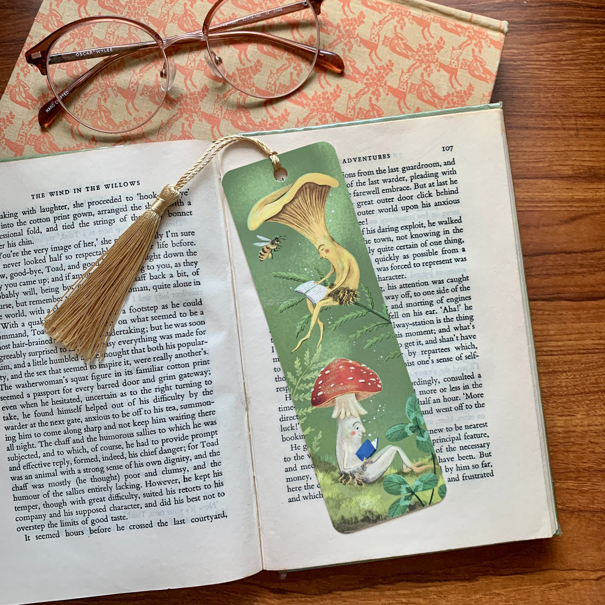 Mushroom Bookclub bookmark by Anna Seed on an open book by glasses, a chanterelle and a red toadstool both reading