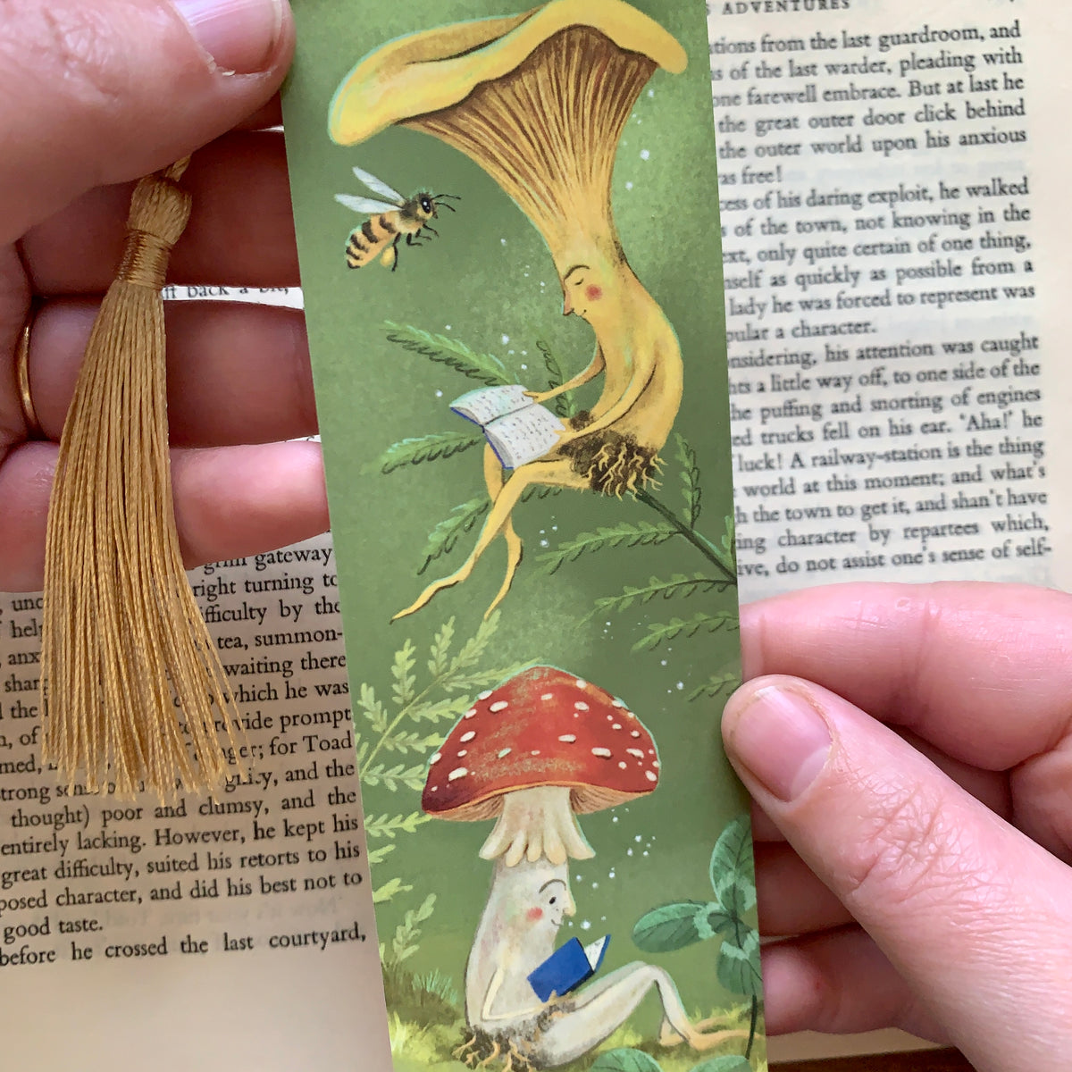 Close-up of the Mushroom Bookclub bookmark held in hand, a yellow chanterelle and spotted toadstool reading books
