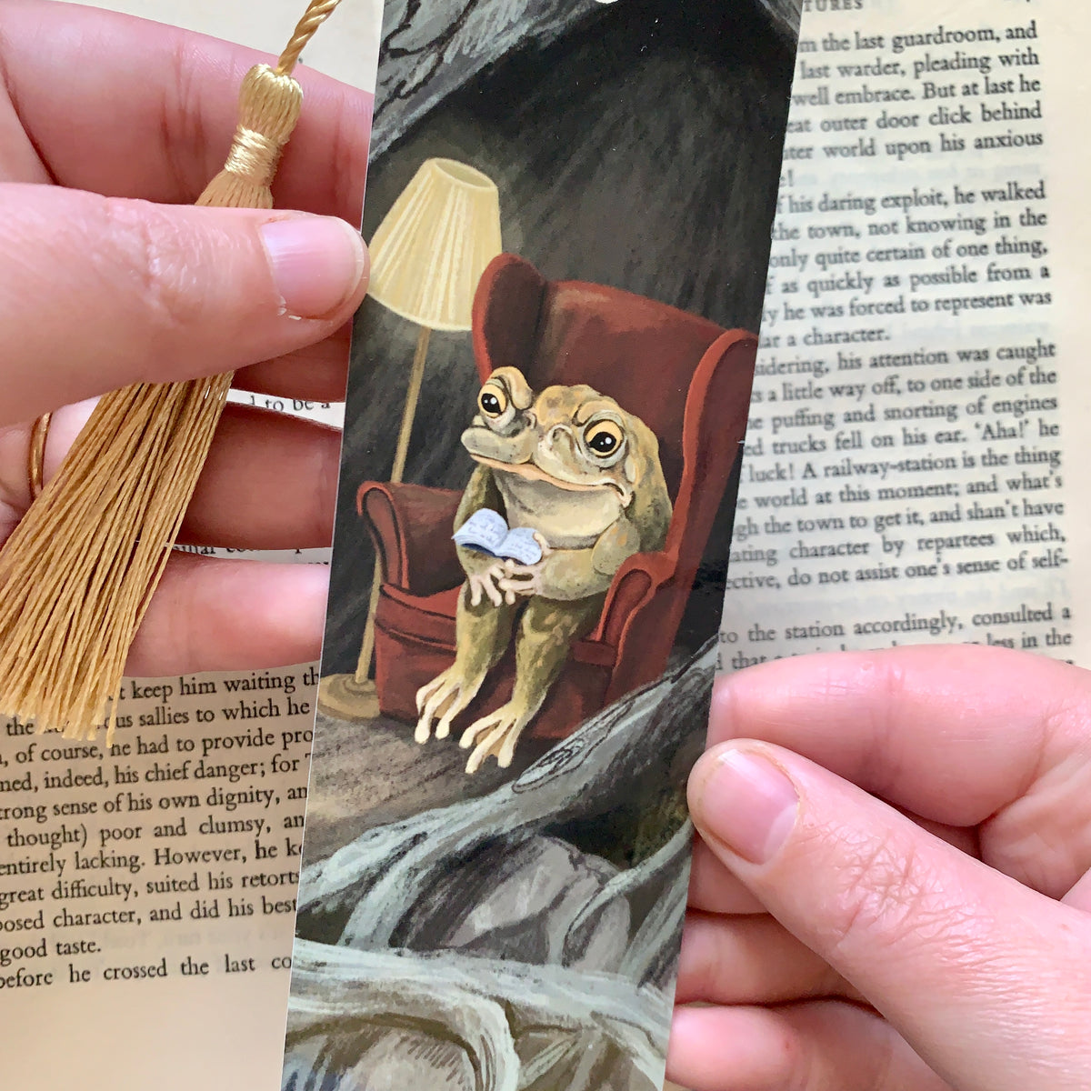 Close-up of the Reading Toad bookmark held in hand, the toad in a red wingback chair with a small book and lamp