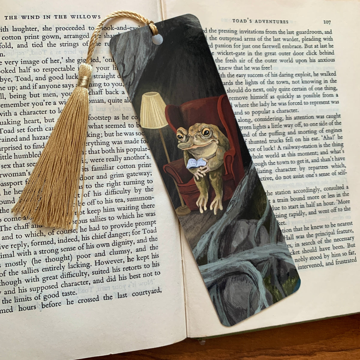 Reading Toad bookmark with a gold tassel lying on the pages of an open book, the toad reading among grey roots