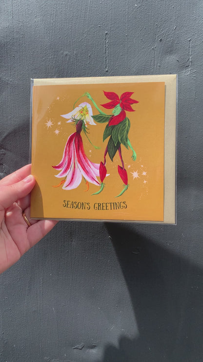 Video: Season's Greetings card with dancing flower characters, held up against a grey wall in sunlight