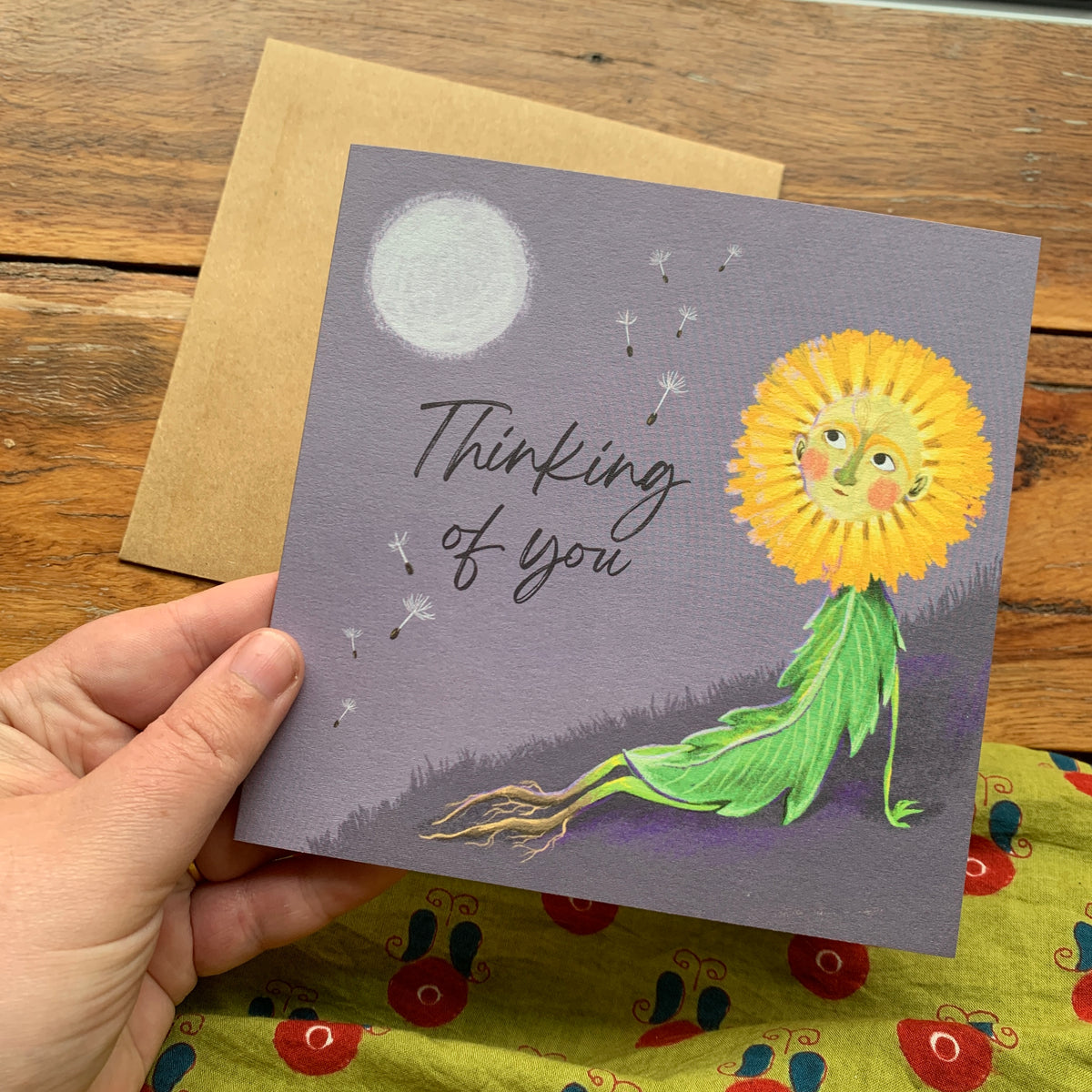 Thinking of you card by Anna Seed: a dandelion character resting on a hill under the full moon, held in hand