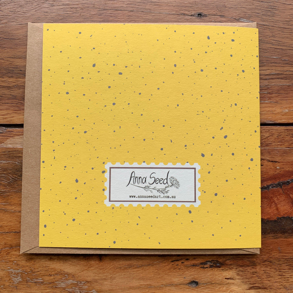 Back of the Thinking of you card in yellow with grey speckles and a stamp-style logo, on a kraft envelope